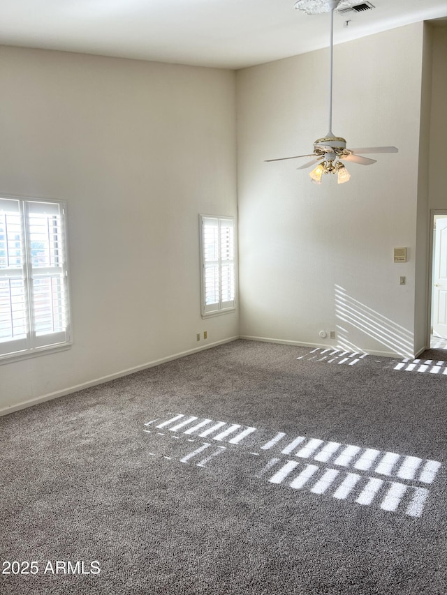 carpeted spare room featuring visible vents, baseboards, a high ceiling, and ceiling fan