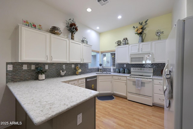 kitchen with visible vents, white cabinets, a sink, white appliances, and a peninsula