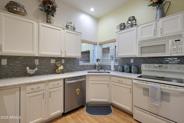 kitchen with white appliances, white cabinetry, a sink, and backsplash