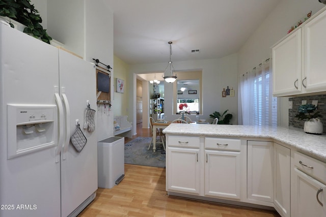 kitchen with a barn door, light wood-style floors, white cabinets, hanging light fixtures, and white fridge with ice dispenser