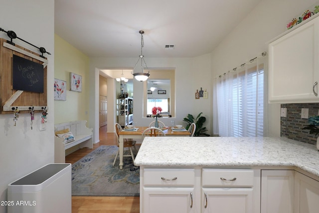 kitchen featuring visible vents, white cabinetry, hanging light fixtures, backsplash, and light stone countertops