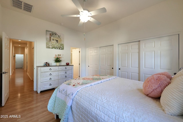 bedroom featuring wood finished floors, visible vents, ceiling fan, and two closets