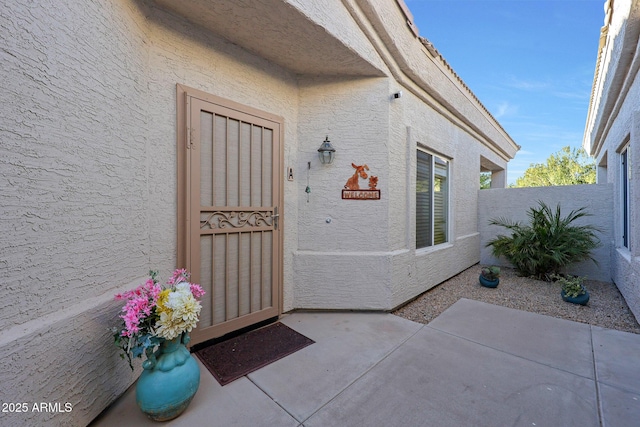 view of exterior entry featuring a patio area, fence, and stucco siding