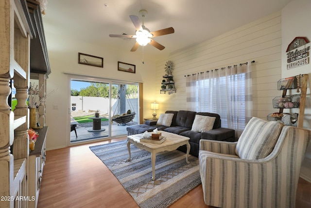 living area with a ceiling fan, wood walls, and light wood finished floors