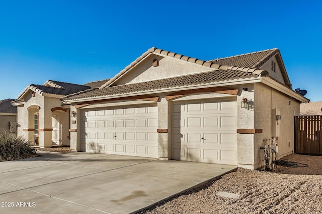 view of property exterior featuring a tile roof, stucco siding, an attached garage, fence, and driveway