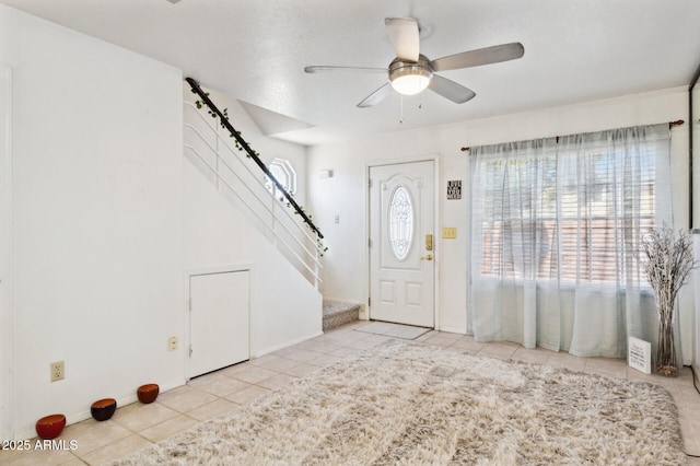 tiled entryway with stairway, ceiling fan, and baseboards