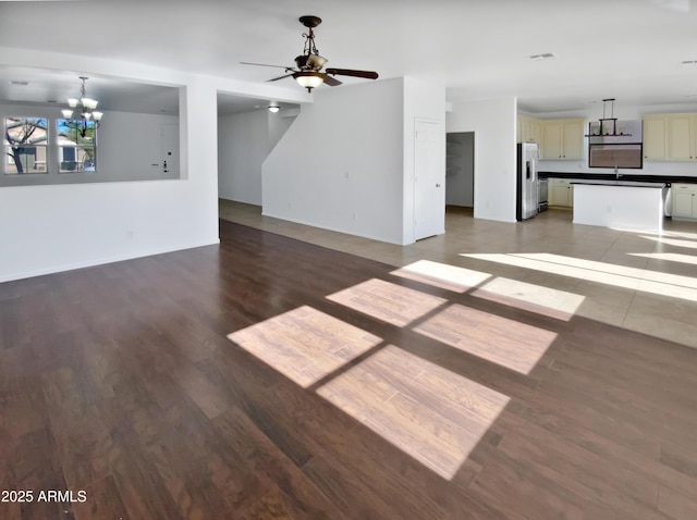 unfurnished living room featuring ceiling fan with notable chandelier, dark hardwood / wood-style flooring, and sink