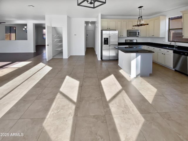 kitchen featuring appliances with stainless steel finishes, a center island, sink, cream cabinets, and decorative light fixtures