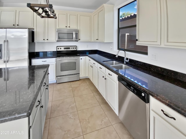 kitchen with sink, decorative light fixtures, light tile patterned floors, dark stone counters, and appliances with stainless steel finishes