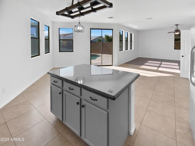 kitchen with pendant lighting, a center island, light tile patterned floors, gray cabinetry, and ceiling fan with notable chandelier