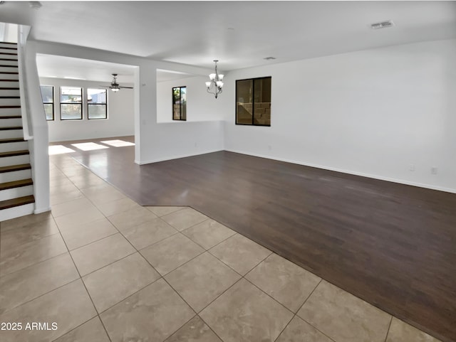 tiled spare room with ceiling fan with notable chandelier