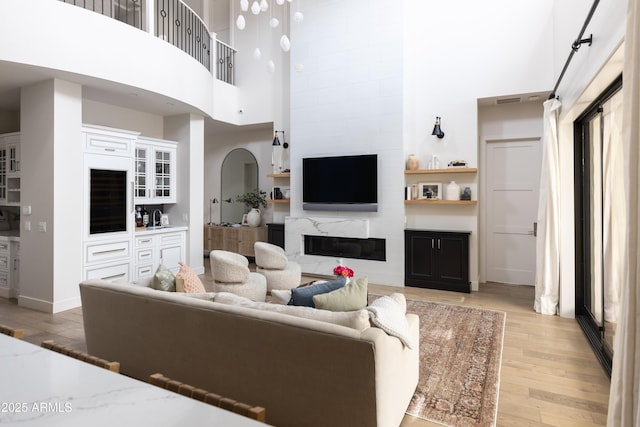 living area featuring a high ceiling, light wood-style floors, a fireplace, and baseboards