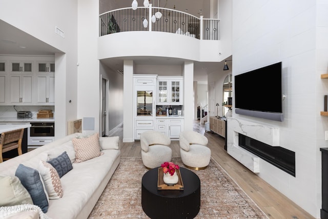 living area with light wood-style flooring, a towering ceiling, and a fireplace