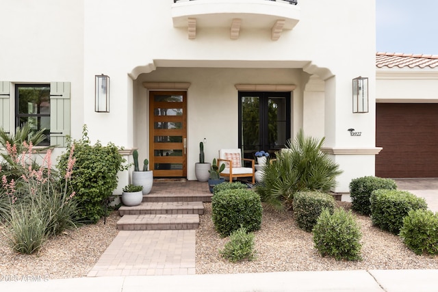 view of exterior entry with french doors, stucco siding, a garage, and a tile roof