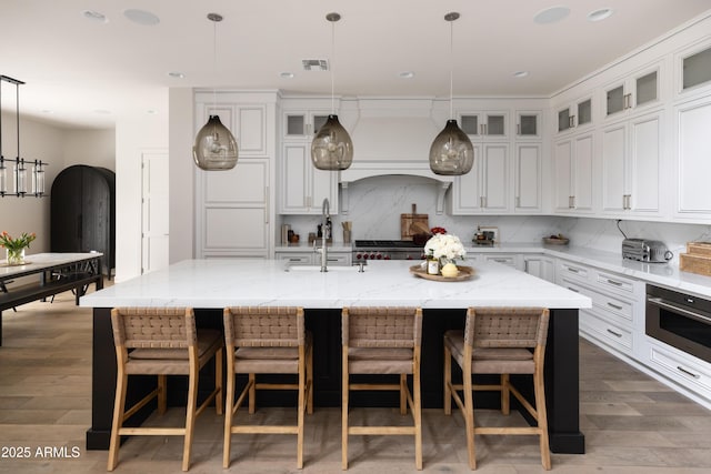 kitchen with stainless steel oven, a sink, wood finished floors, white cabinetry, and a spacious island
