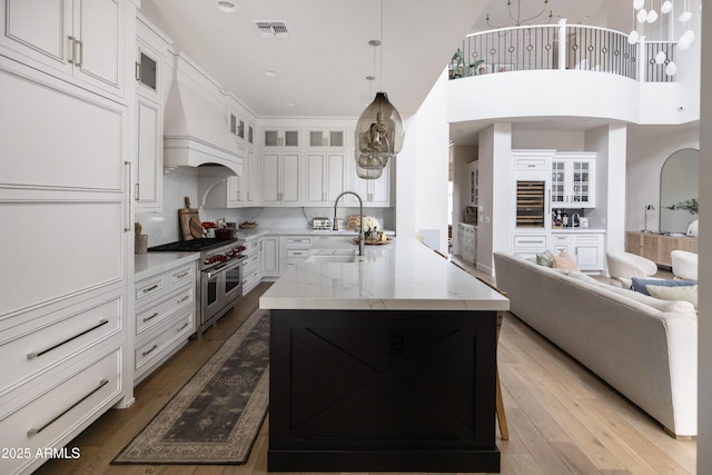 kitchen with range with two ovens, open floor plan, a sink, white cabinets, and light stone countertops