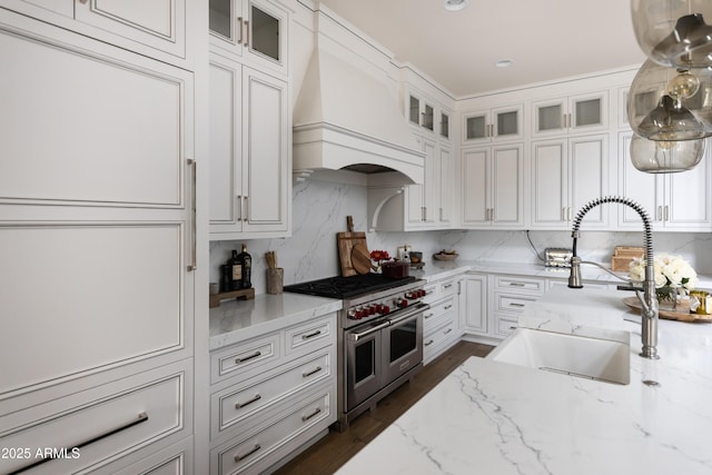kitchen with double oven range, a sink, white cabinetry, premium range hood, and decorative backsplash