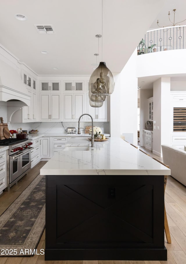 kitchen featuring range with two ovens, a sink, white cabinets, light stone counters, and glass insert cabinets