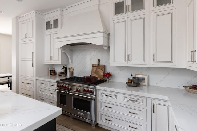kitchen with range with two ovens, custom exhaust hood, white cabinets, tasteful backsplash, and light stone countertops