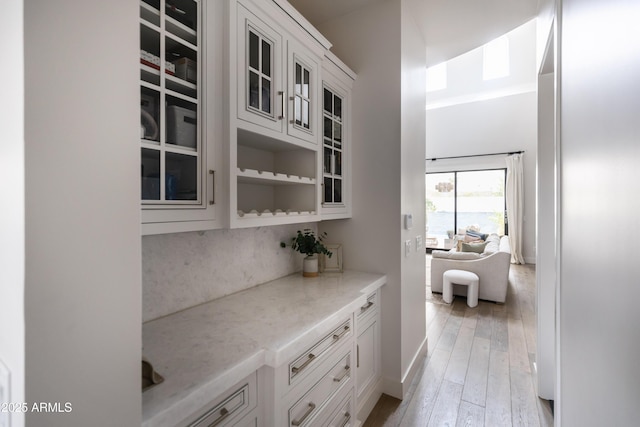 bar with light wood-type flooring, backsplash, and baseboards