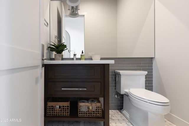 half bathroom featuring toilet, vanity, tile walls, and a wainscoted wall