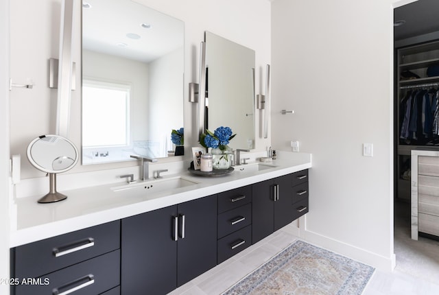 bathroom featuring double vanity, a walk in closet, and baseboards