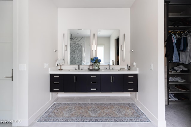 full bath with a spacious closet, double vanity, a walk in shower, and baseboards