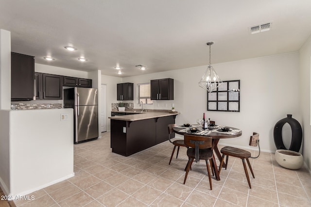 kitchen featuring hanging light fixtures, light tile patterned floors, a breakfast bar area, a notable chandelier, and stainless steel fridge