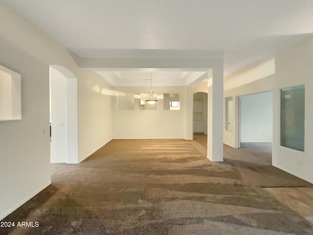 unfurnished room featuring carpet, a raised ceiling, and a chandelier