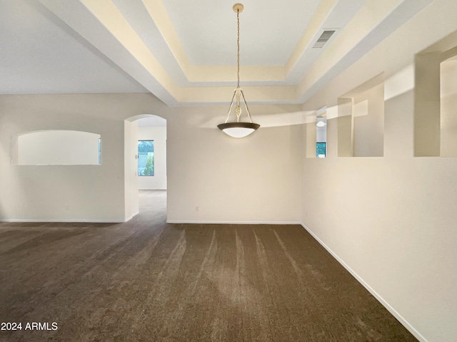 spare room with a tray ceiling and dark colored carpet