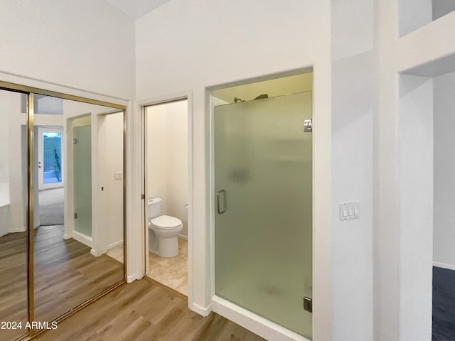 bathroom with hardwood / wood-style floors, toilet, and a shower with door