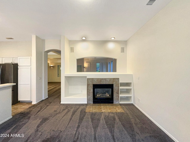 unfurnished living room with dark carpet and a tiled fireplace