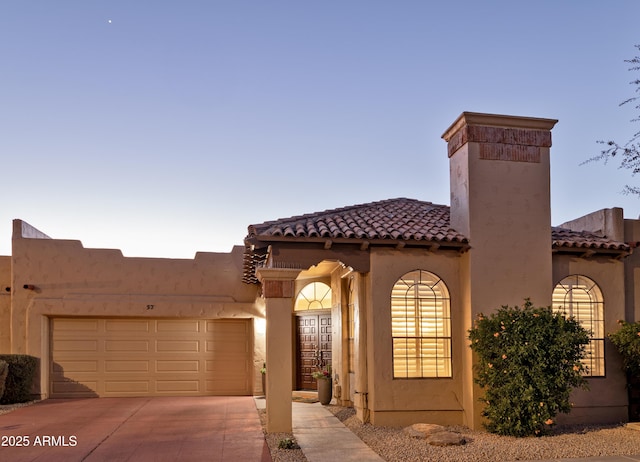 view of front facade featuring driveway, a chimney, an attached garage, and stucco siding