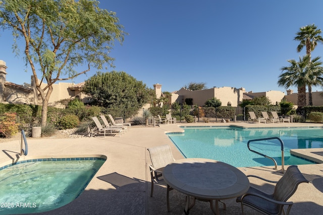 pool with a patio area, fence, and a hot tub