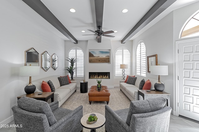 living room with baseboards, a glass covered fireplace, beam ceiling, and a healthy amount of sunlight