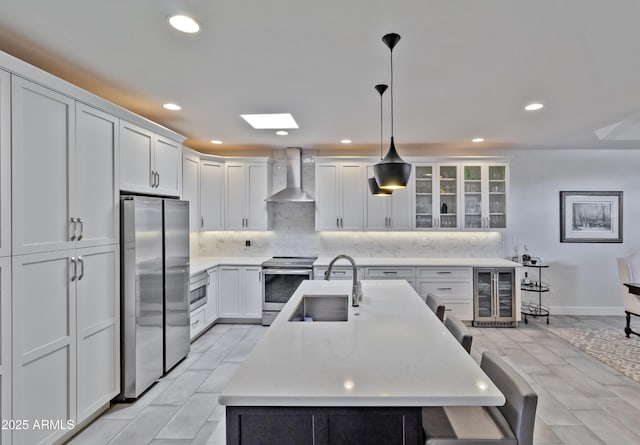 kitchen featuring wall chimney exhaust hood, wine cooler, a sink, stainless steel appliances, and backsplash