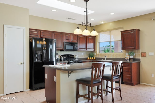 kitchen featuring decorative backsplash, an island with sink, black appliances, decorative light fixtures, and sink