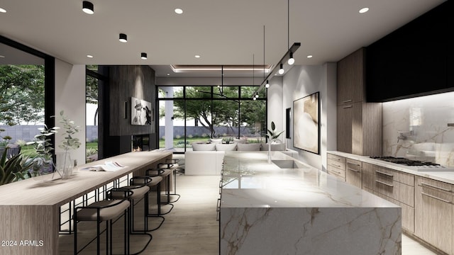 kitchen with stainless steel gas stovetop, a kitchen bar, hanging light fixtures, a large island, and light stone counters