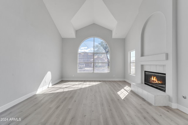 unfurnished living room featuring light hardwood / wood-style floors, vaulted ceiling, and a tiled fireplace