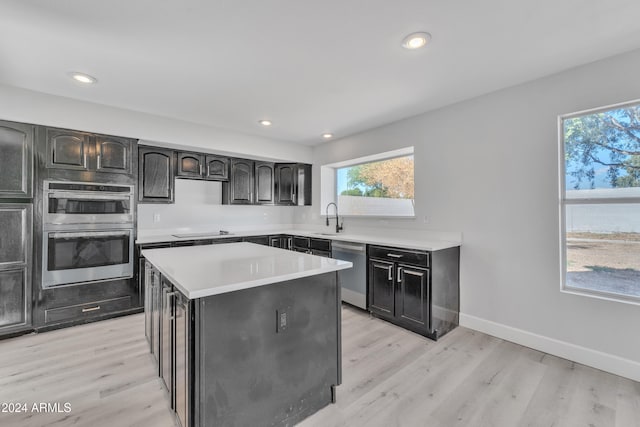 kitchen with appliances with stainless steel finishes, light wood-type flooring, a kitchen island, and sink