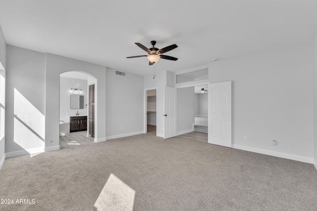 unfurnished bedroom featuring a walk in closet, ensuite bath, ceiling fan, light colored carpet, and a closet