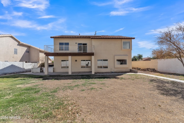 rear view of house with a balcony, a patio area, and a lawn