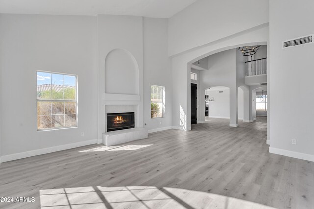 unfurnished living room with light hardwood / wood-style floors, a towering ceiling, and an inviting chandelier