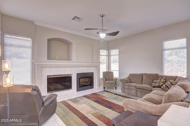 tiled living room with ceiling fan, a healthy amount of sunlight, and a tiled fireplace