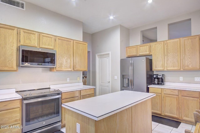 kitchen featuring light tile patterned flooring, light brown cabinetry, a center island, appliances with stainless steel finishes, and a high ceiling