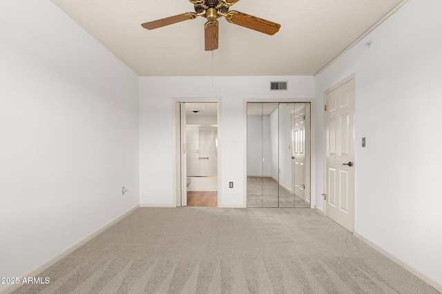 unfurnished bedroom featuring ceiling fan, light colored carpet, a textured ceiling, and ensuite bath