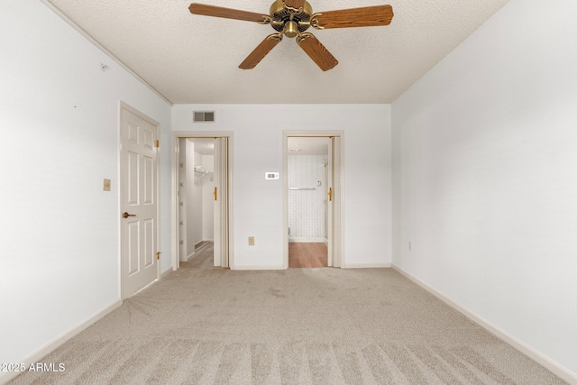 unfurnished bedroom featuring connected bathroom, a walk in closet, light carpet, a textured ceiling, and ceiling fan