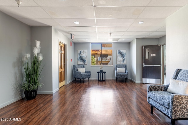 living area with dark wood-type flooring and a paneled ceiling