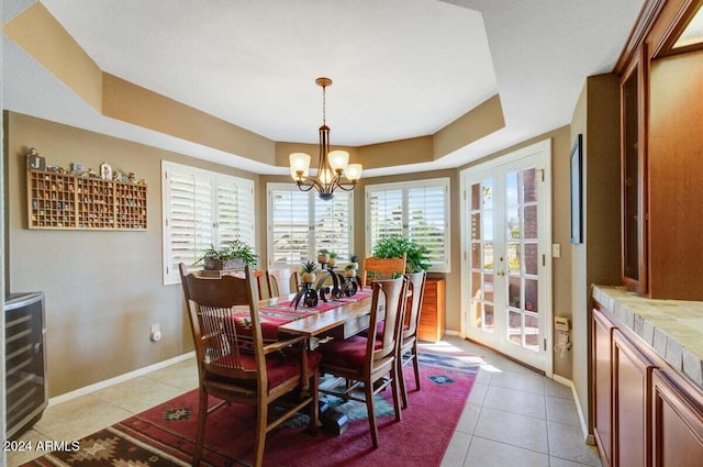 tiled dining space featuring a notable chandelier, a raised ceiling, wine cooler, and french doors