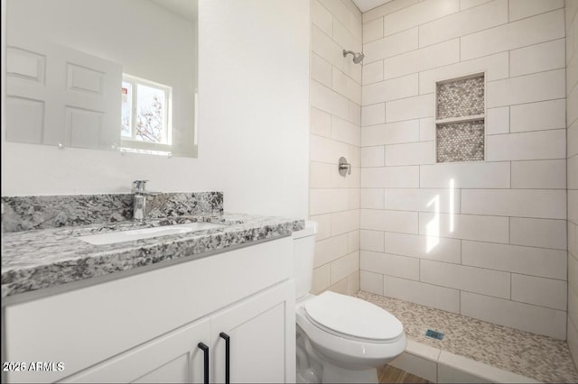 bathroom with vanity, toilet, and tiled shower